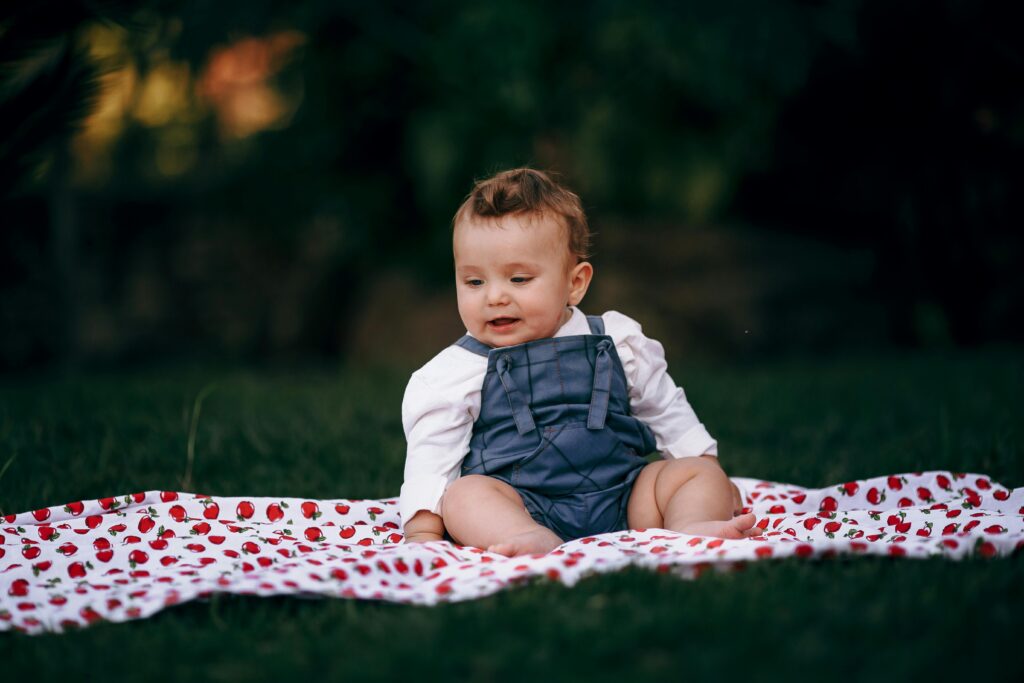 Charming baby enjoying a relaxing moment on a strawberry-patterned blanket in a park setting.