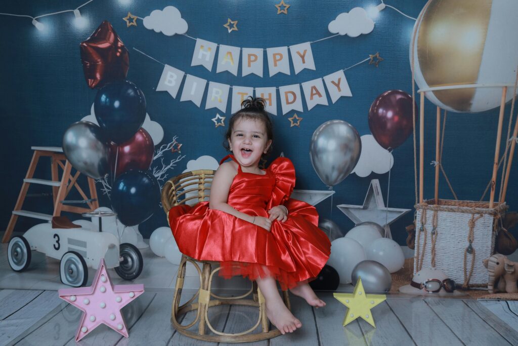 Joyful baby girl celebrating her first birthday with balloons and decorations indoors.